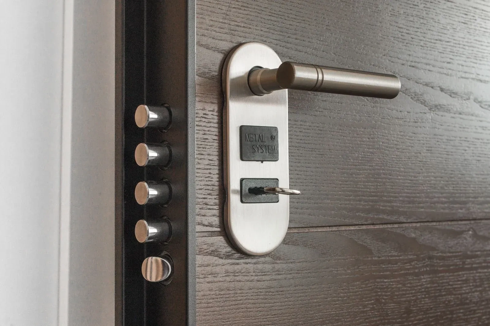 Steel door lever on an oval plate with a key in the lock, beside a row of metal bolts on the edge. — Brampton